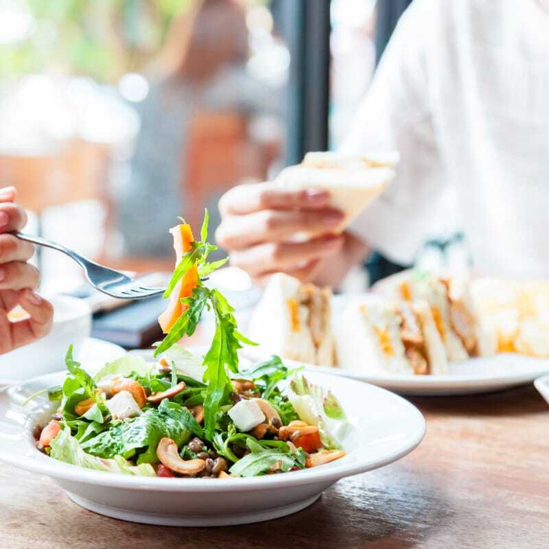 Close-up of a salad dish with hands reaching for food