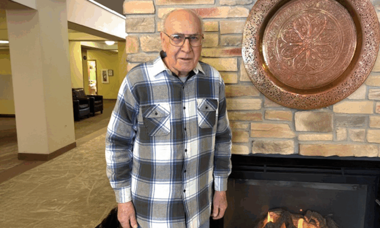 Senior resident standing in a common area by a fireplace