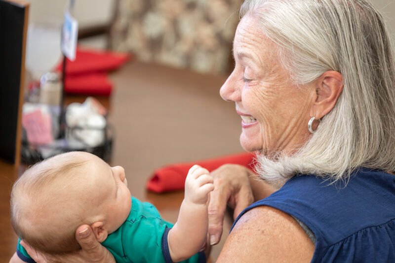 A senior woman smiling and holding a baby