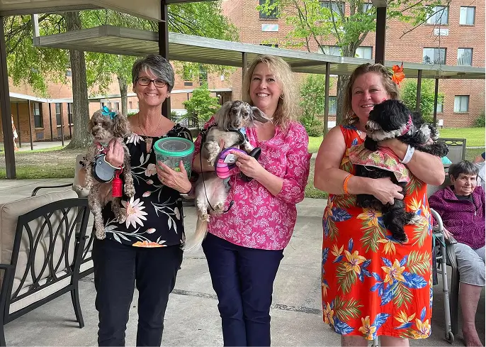 Staff and residents holding small dogs in an outdoor setting