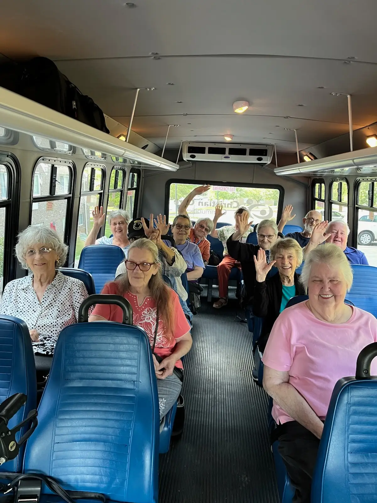 Residents on a facility transport bus, waving happily