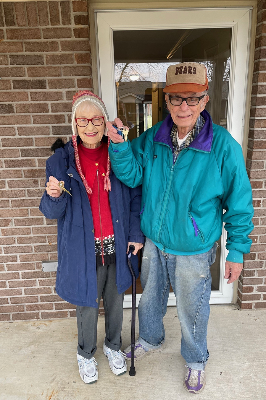 Two residents holding keys in front of a building entrance