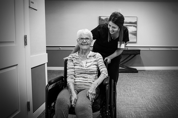 A caregiver assisting a smiling resident in a hallway