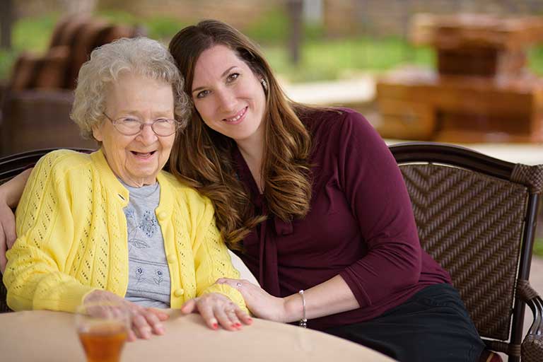 Smiling elderly resident with staff in outdoor setting