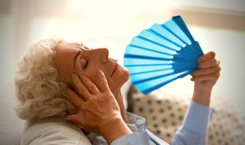 A senior woman relaxing with a fan indoors