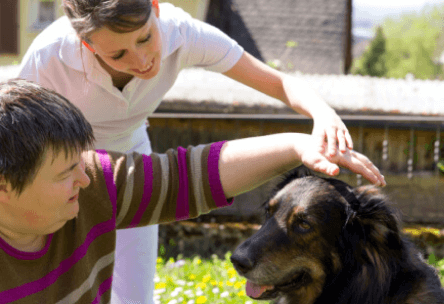 A caregiver and resident interacting with a dog outdoors.