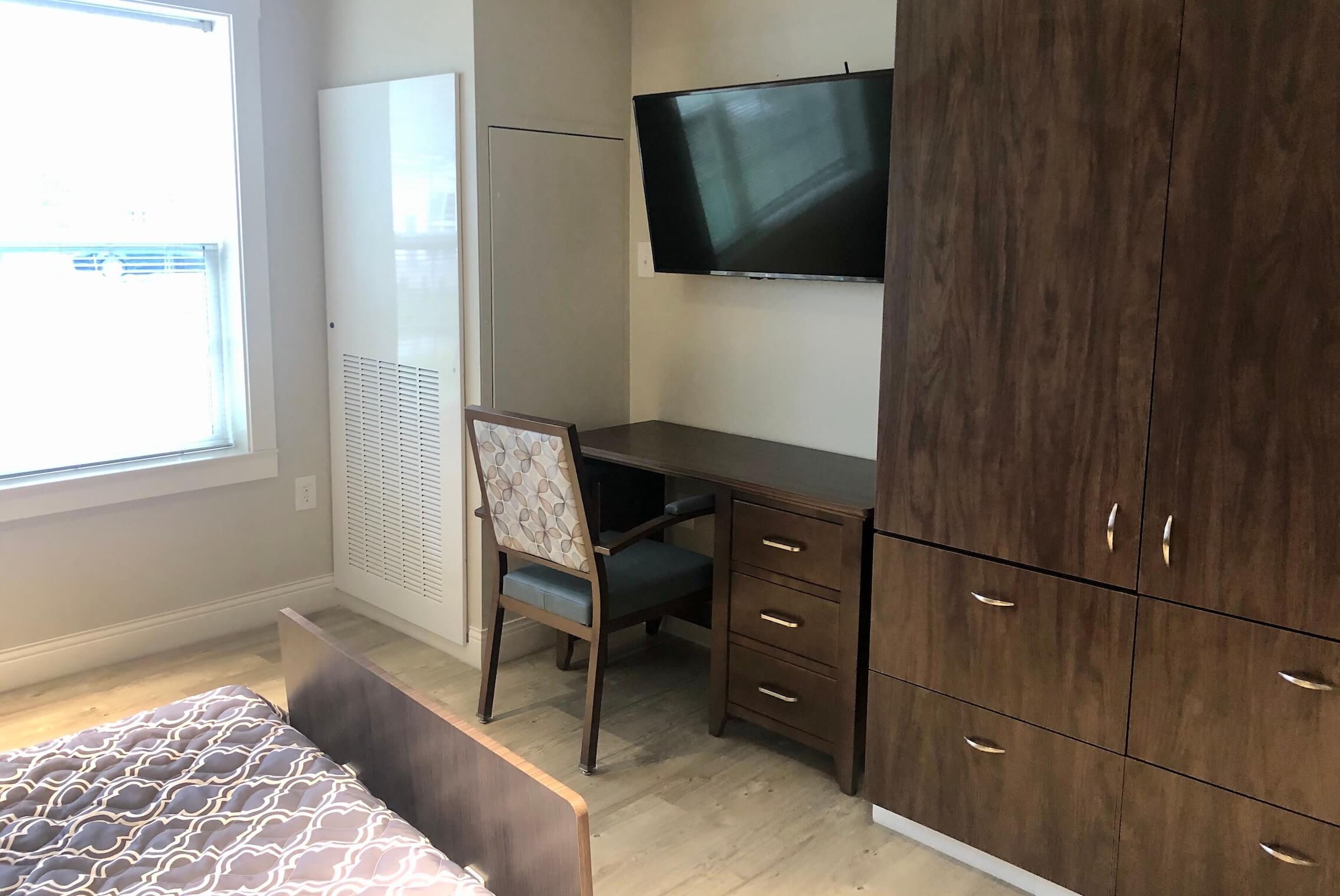 Neatly arranged resident room interior with furniture and TV.