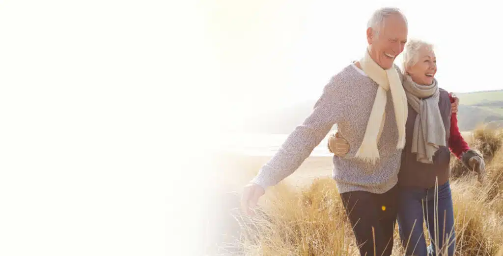 An elderly couple walking outdoors in a natural setting.