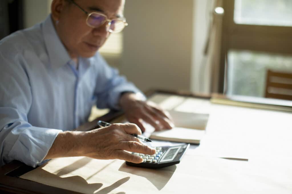 Senior man using a calculator at a table.