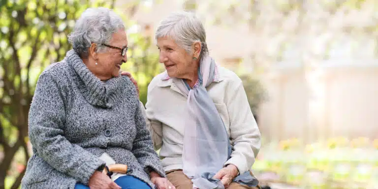 Two elderly women engaging in conversation outdoors.
