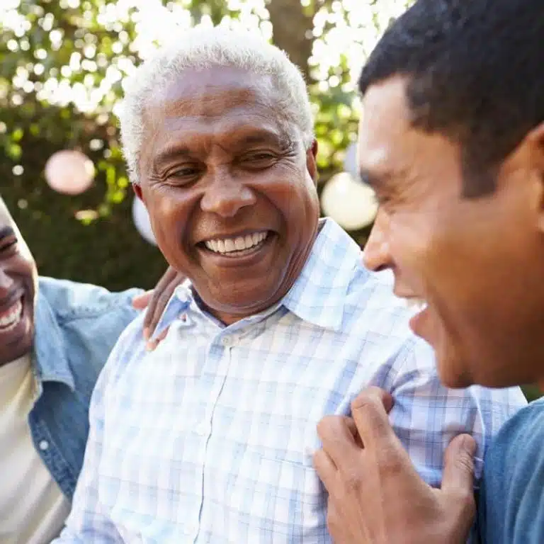 Smiling elderly man surrounded by two younger men outdoors