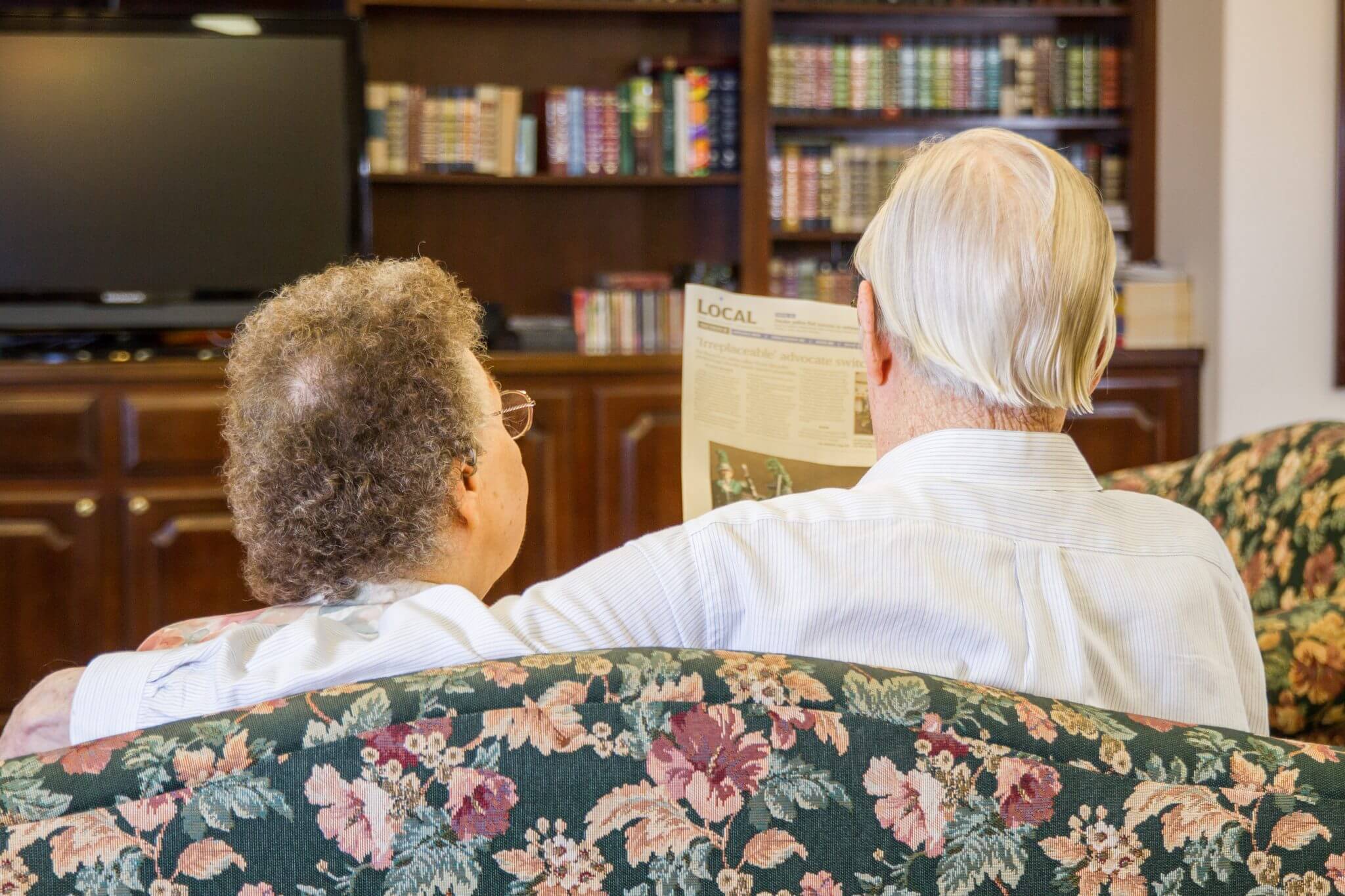 Two residents reading a newspaper on a couch.
