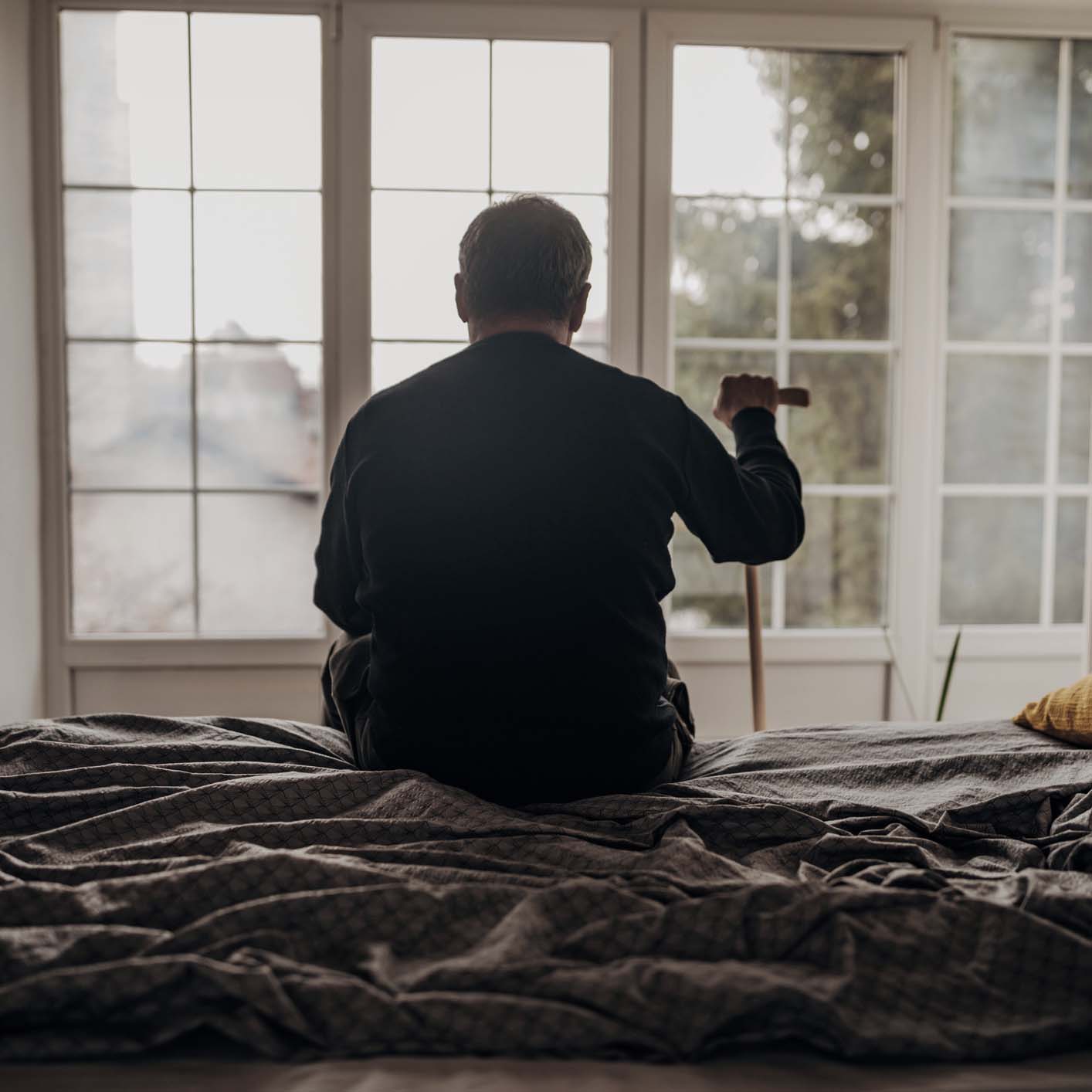 Senior man sitting on a bed, looking out the window