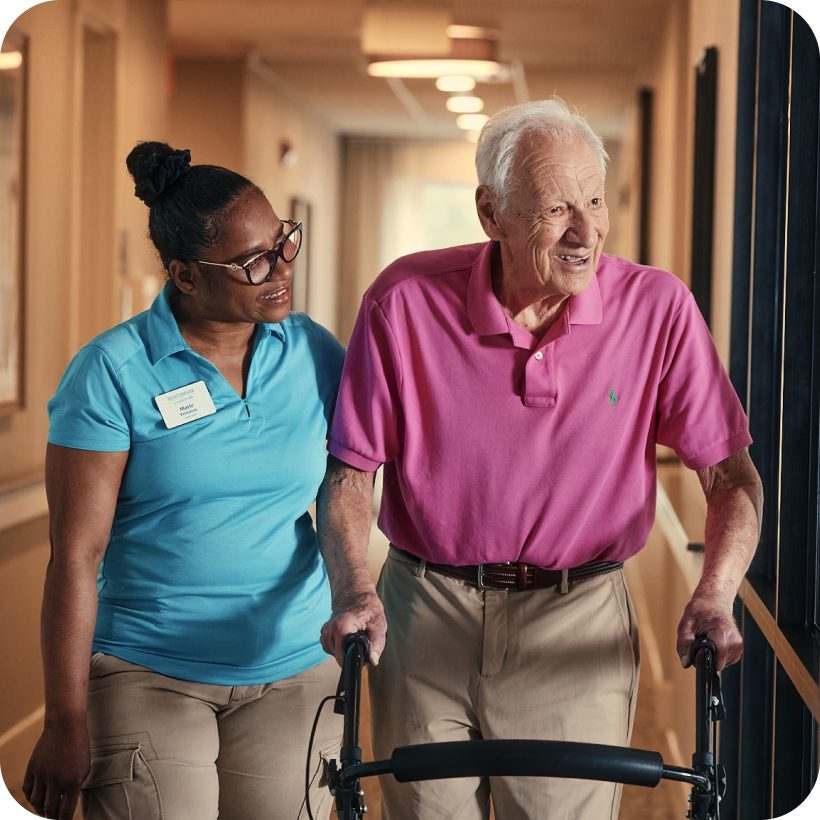 Staff assisting an elderly resident in a hallway.