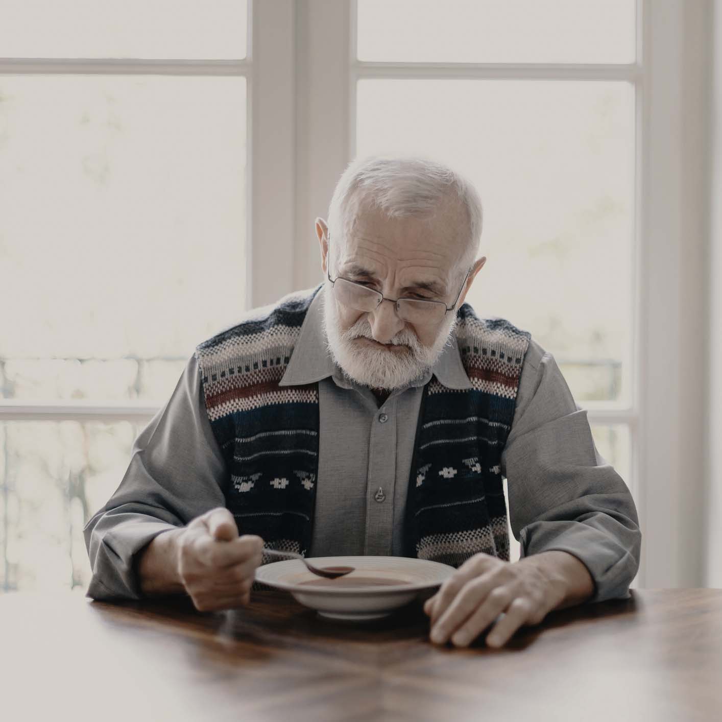 Elderly man sitting at a table with a bowl.
