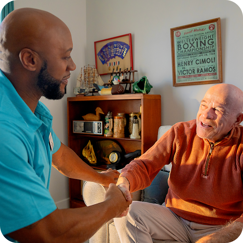 A caregiver and resident shaking hands in a cozy interior.
