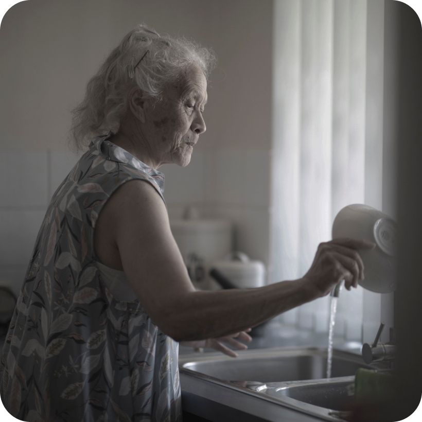 Elderly woman washing dishes at the sink.