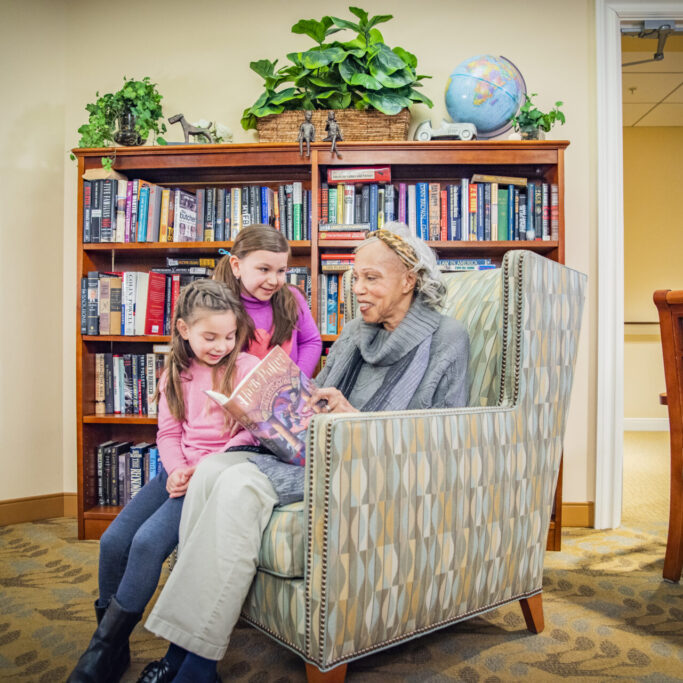 Senior resident reading with children in a cozy library setting.