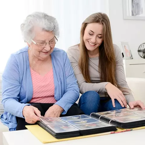 Senior woman and young adult looking at a photo album together.