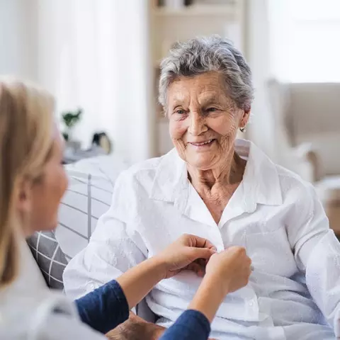 Smiling elderly woman interacting with caregiver indoors.