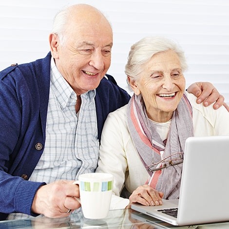 Two seniors happily using a laptop together.