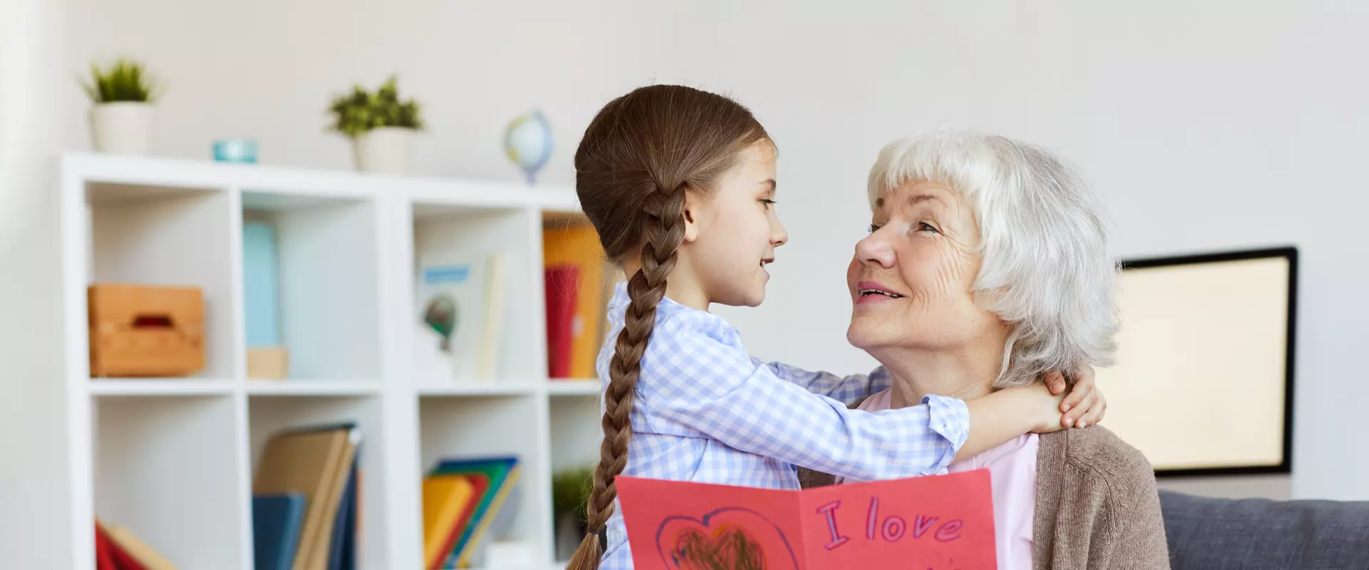 Child with a drawing embraces an elderly woman.