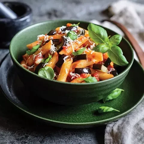 A bowl of pasta with vegetables and basil.