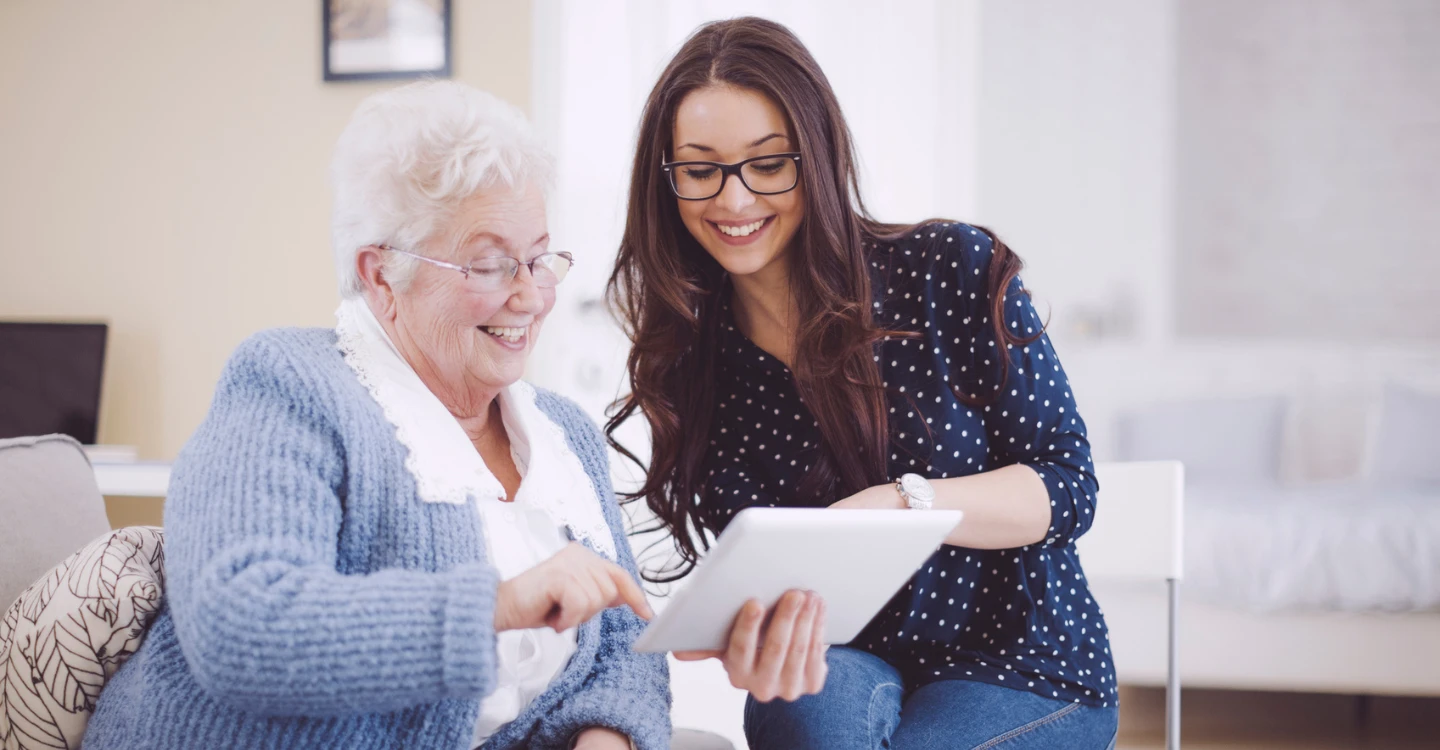 Senior resident and staff member using a tablet together.