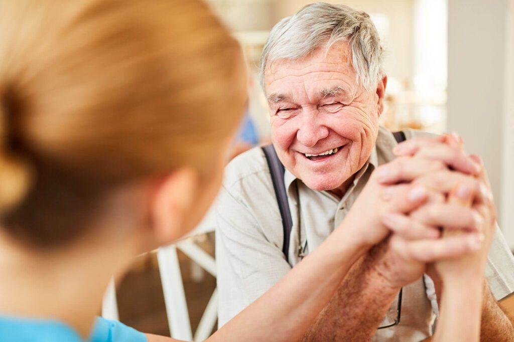 Senior man smiling while holding hands with caregiver.