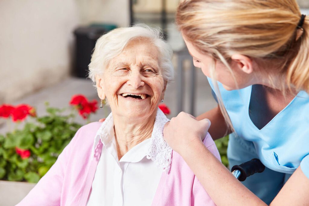 Caregiver interacting with smiling elderly resident outdoors.