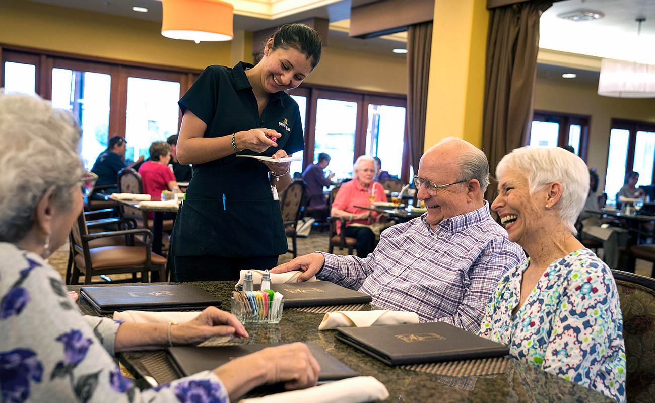 Happy residents enjoying a meal with staff in the dining area.