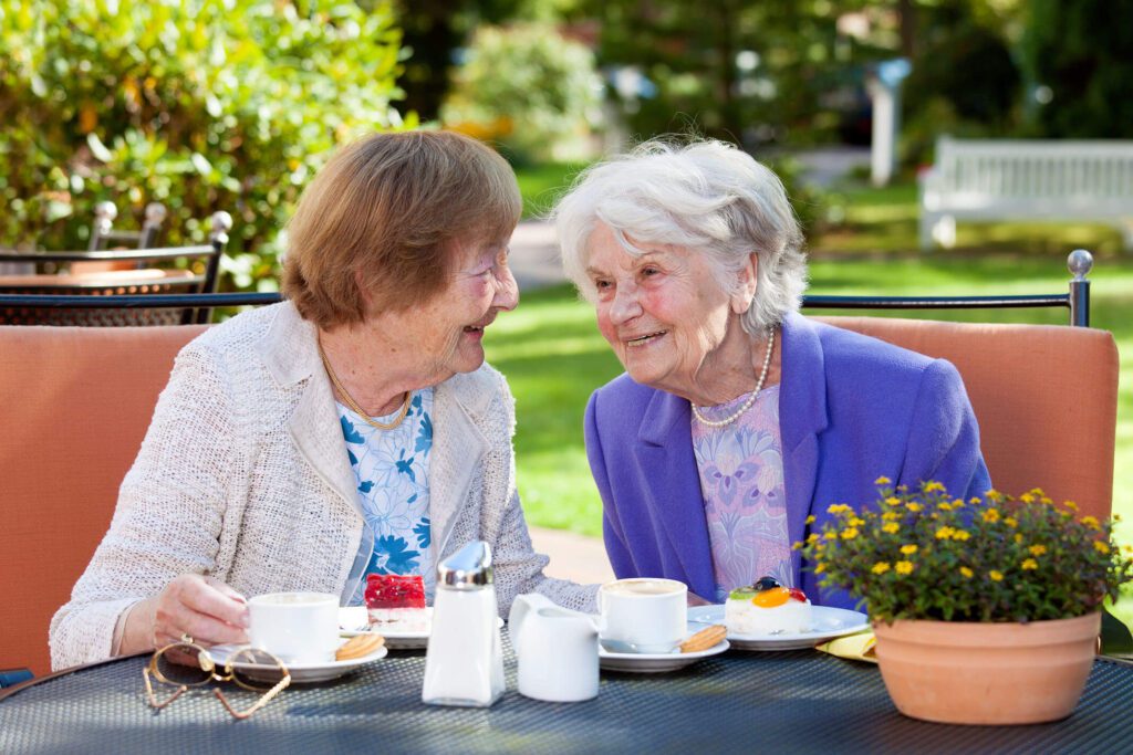 Two elderly women enjoying tea outdoors.