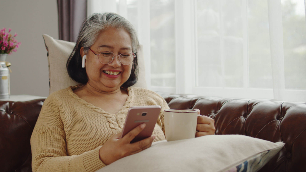 Senior woman enjoying tea and using a smartphone.