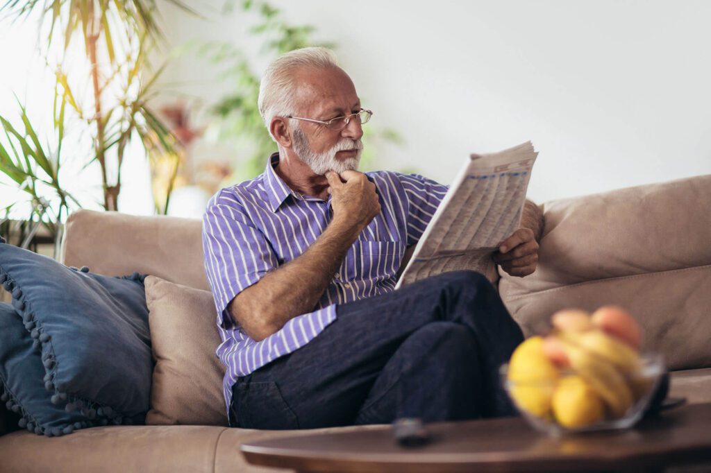 Senior man reading newspaper in living area.
