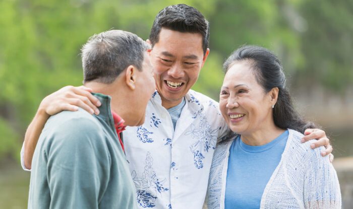 Three smiling individuals enjoying outdoor conversation.