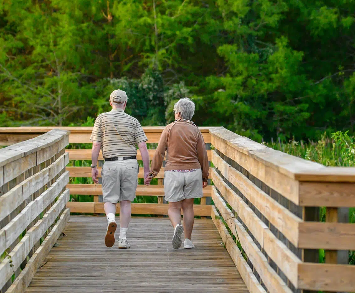Seniors walking hand in hand on a wooden bridge.