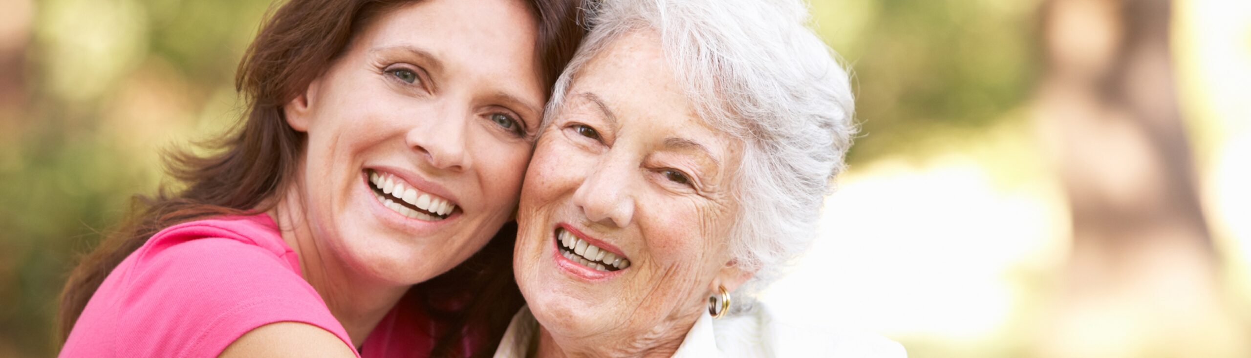 Two women smiling outdoors, embracing each other.