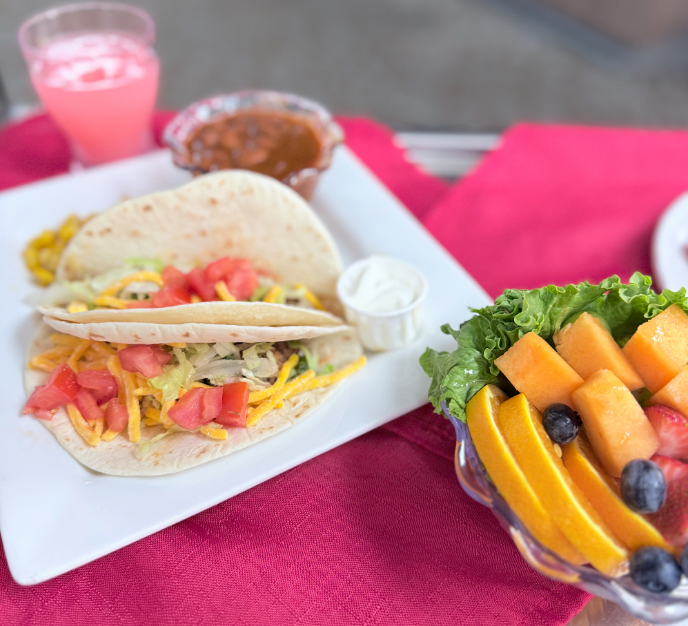 A plate of tacos with fruit and drink