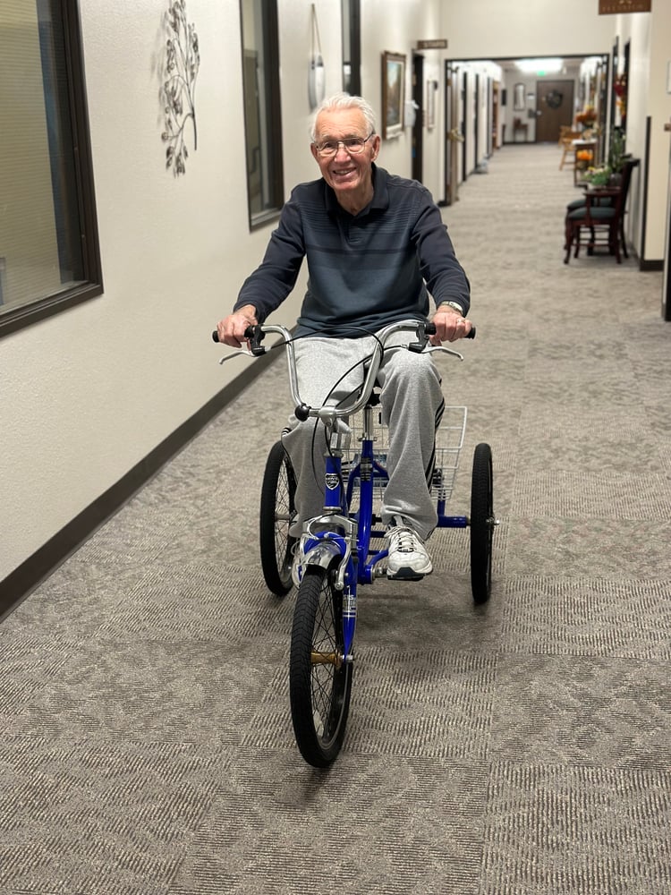An elder man riding a tricycle in a hallway.
