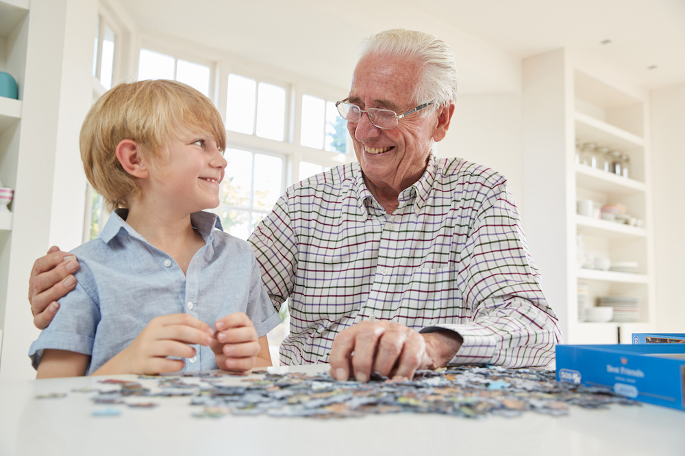 Elderly man smiling with a young boy over a puzzle