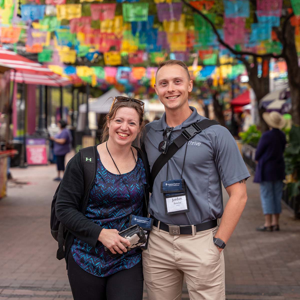 Two people smiling at an outdoor event with colorful decorations.