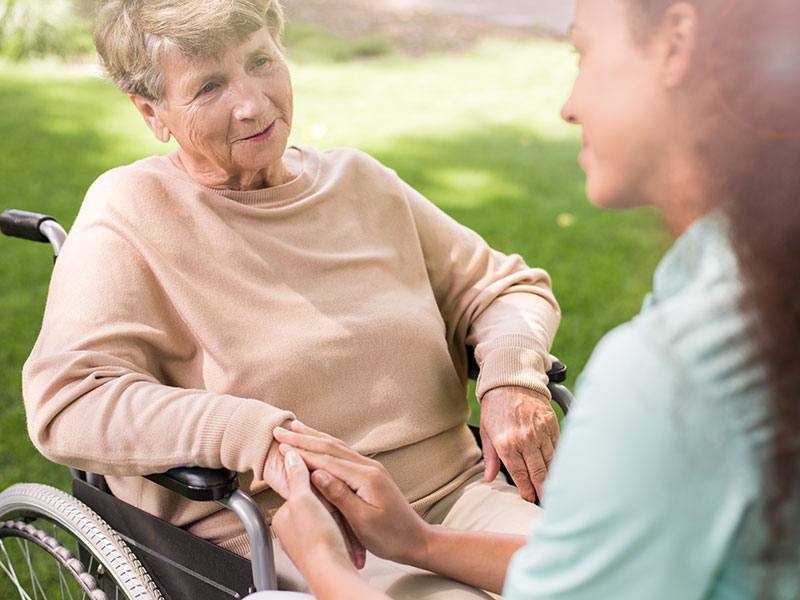 Senior woman in a wheelchair with caregiver outside.
