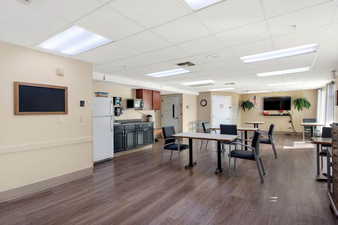 Common area with tables and chairs in a bright room.