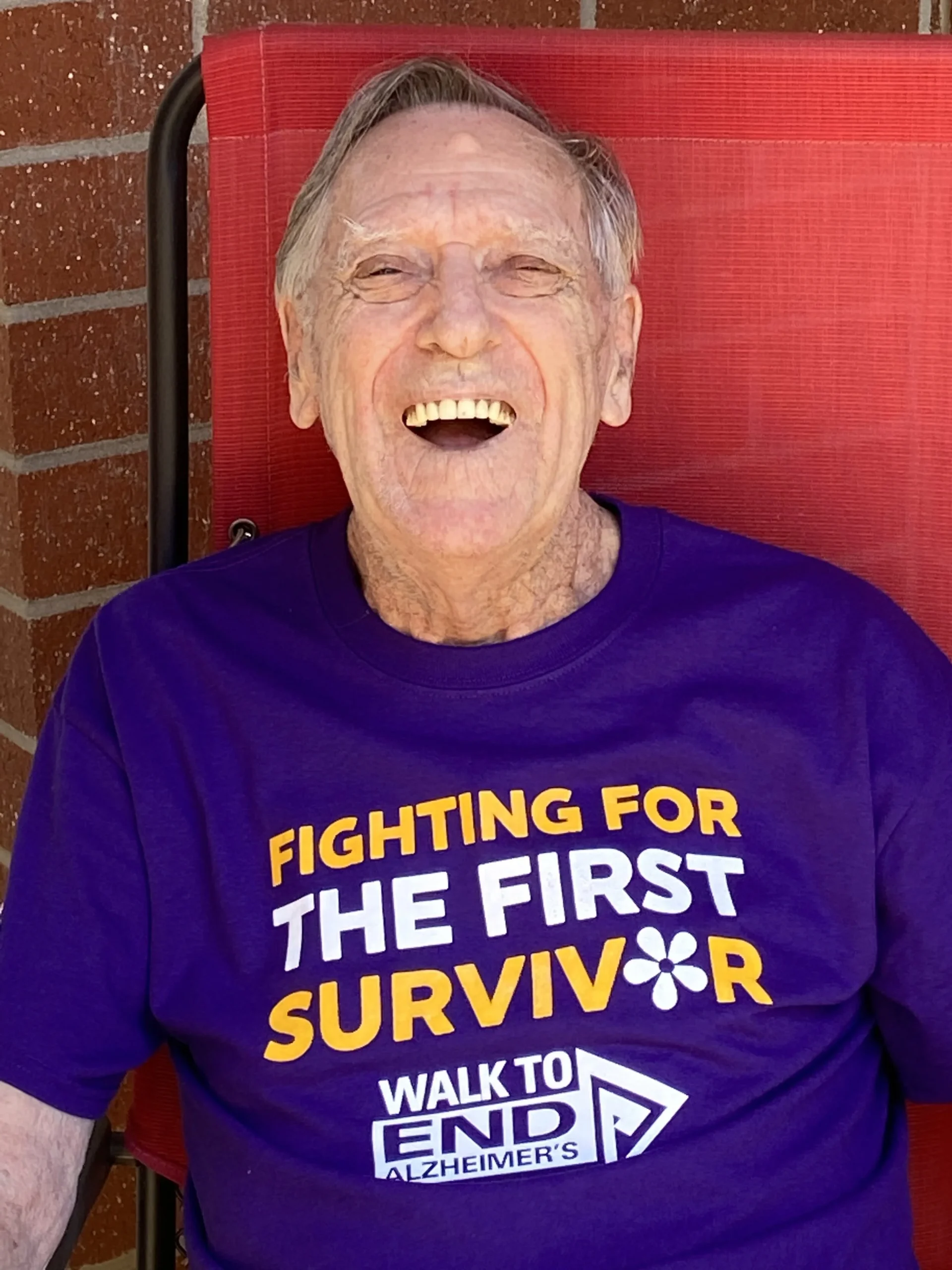 Senior man smiling in a purple charity t-shirt outdoors.