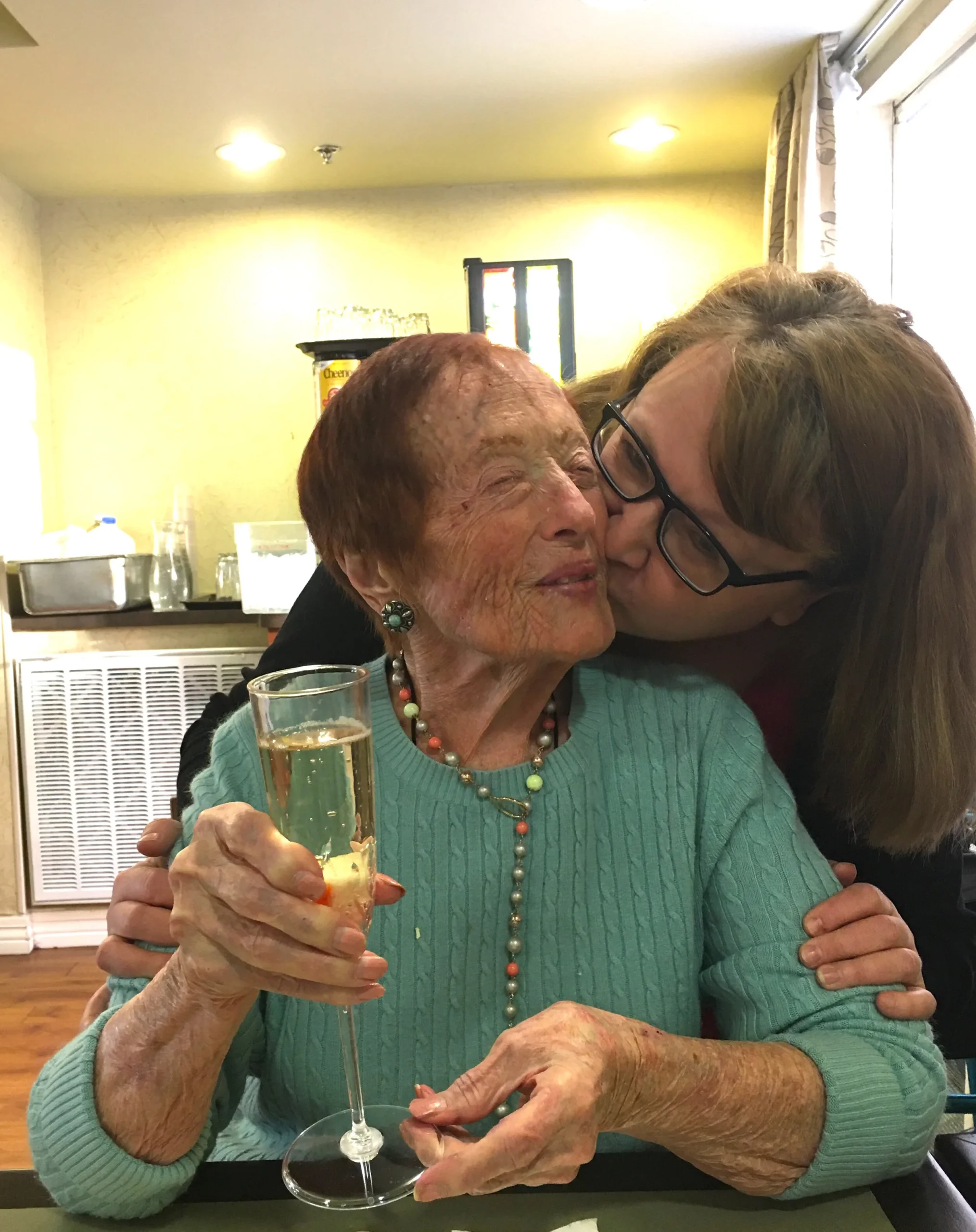 A caregiver kisses a resident while holding a drink.