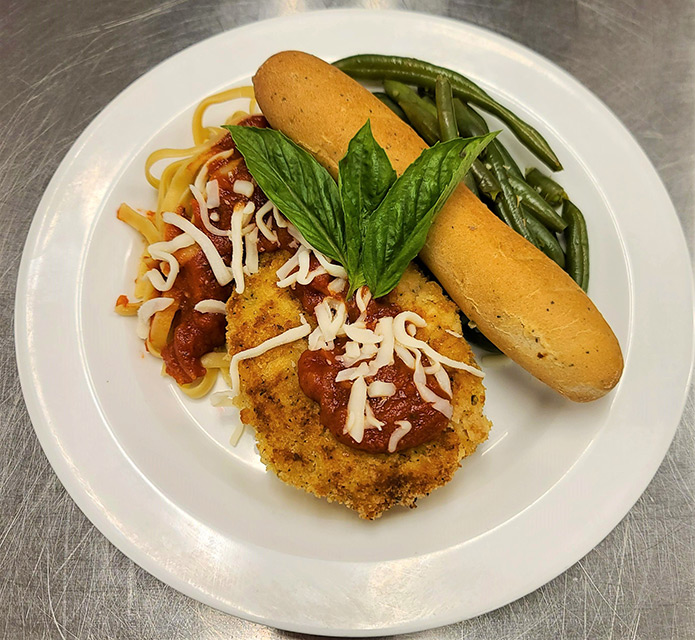 Plate of pasta with chicken, green beans, and breadstick