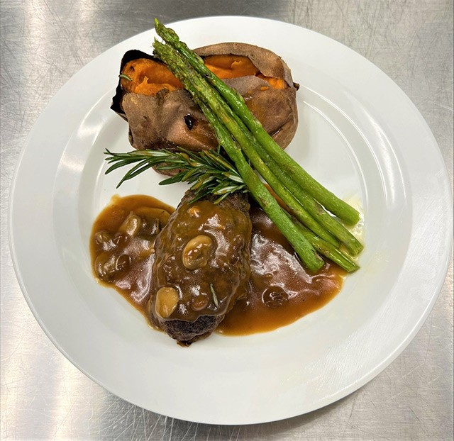 A plated dinner with meat, asparagus, and a sweet potato