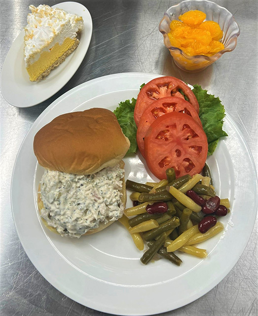 A plated meal with sandwich, vegetables, and dessert