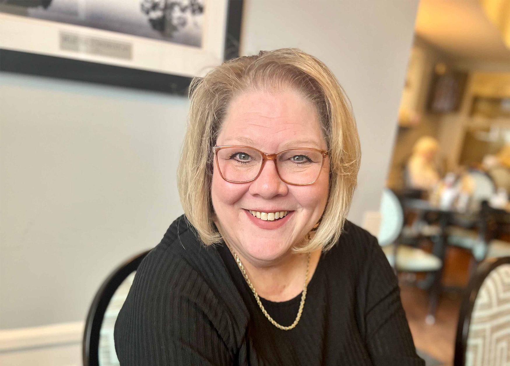 Smiling woman in a dining area with other people in the background