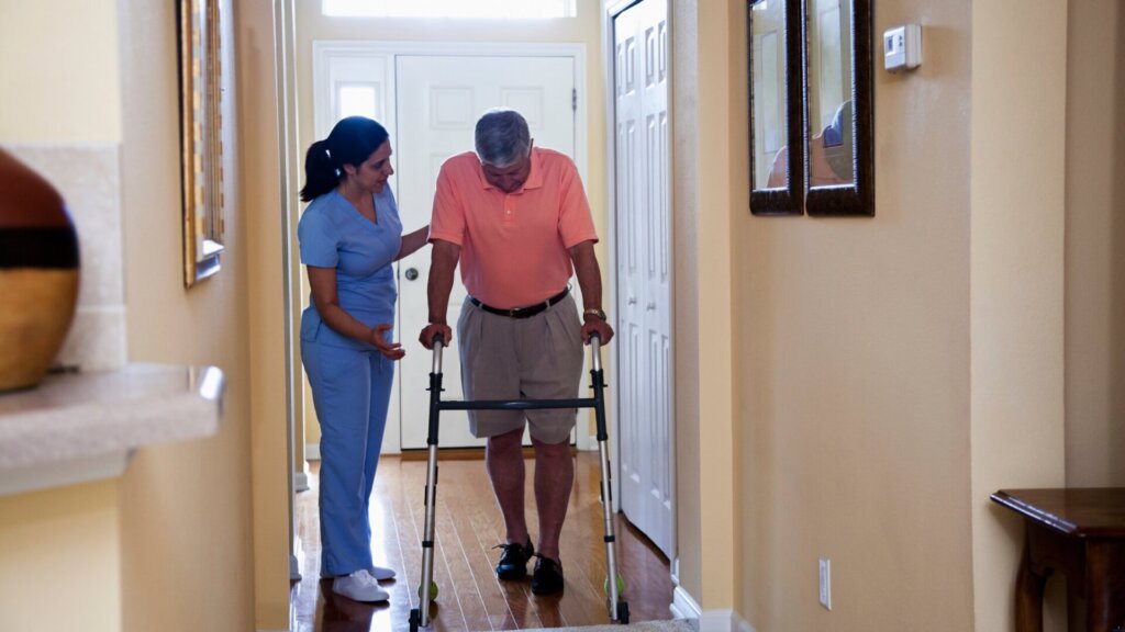 Caregiver assisting a resident with a walker in a corridor